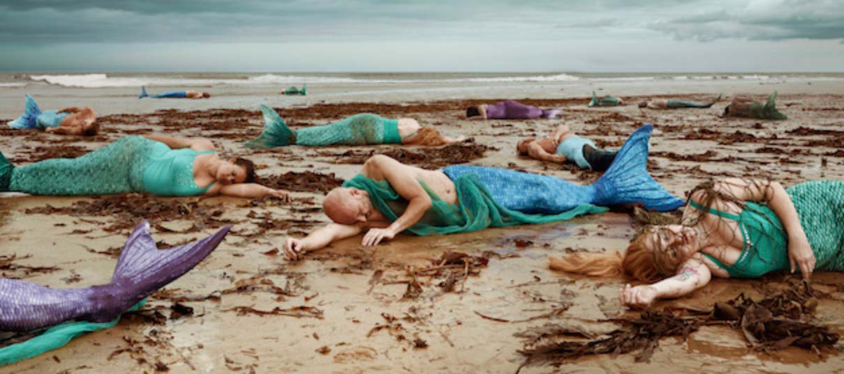 Humans with fishtails lying on a beach